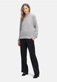 Hellgrauer, gestrickter Pullover mit hohem Kragen und lockerer Passform; verfügt über ein strukturiertes Muster. Kombiniert mit schwarzen, weit geschnittenen Hosen und Stiefeletten.