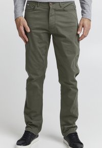 Olijfgroene katoenen chinos met een rechte snit, voorzakken en een rode knop. Gepaarde met zwarte sneakers met een witte zool.