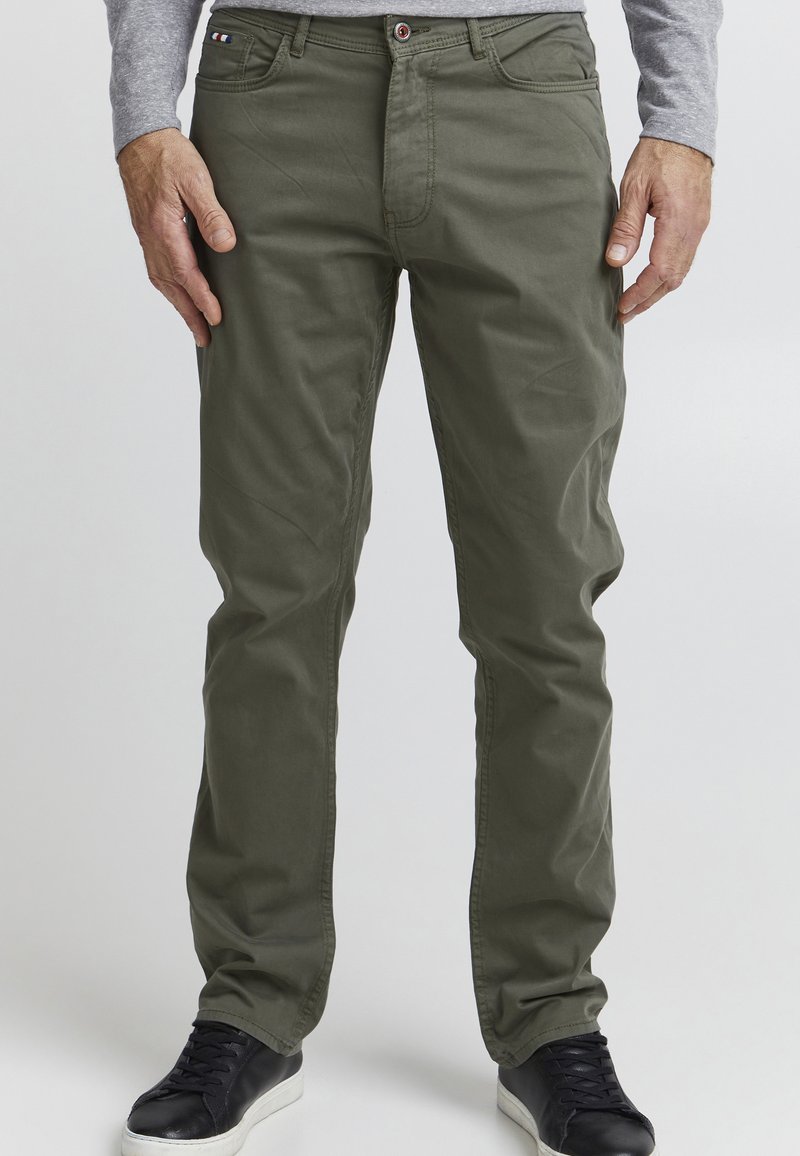 Olijfgroene katoenen chinos met een rechte snit, voorzakken en een rode knop. Gepaarde met zwarte sneakers met een witte zool.