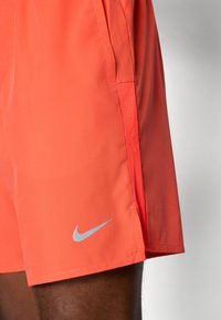 Nike-short i livlig korall, med ett mjukt, lätt material, sidopaneler i mesh förandningsförmåga och en silverfärgad logotypdetalj.