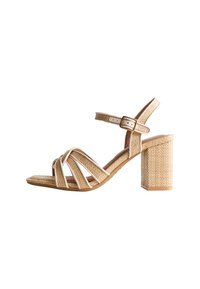 Beige strappy sandal with a block heel, featuring woven texture and white accents. Adjustable ankle strap with a metallic buckle.