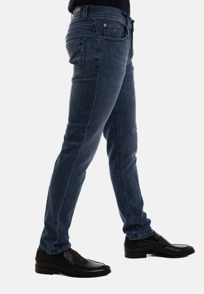 Jeans blu a taglio slim con lavaggio sbiadito, dotati di cinque tasche e scarpe di pelle nera, mostrati in profilo laterale su uno sfondo neutro.