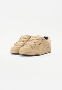 Tan low-top sneakers with textured leather, featuring round laces, a padded collar, and a black inner lining. Rubber sole with accent details.