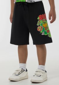 Pantaloni corti neri in cotone con una vita elasticizzata, caratterizzati da una stampa grafica colorata di un personaggio verde e fette di pizza sul lato sinistro.