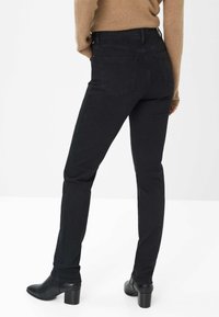 Jeans in denim nero con una vestibilità slim, dotati di tasche posteriori e una vita alta. Abbinati a un maglione beige e stivali alla caviglia.