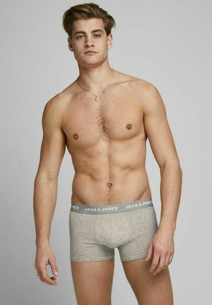Graue Baumwollboxershorts mit einem elastischen Bündchen mit Logo. Das Modell steht selbstbewusst da und präsentiert die Passform und das Design.