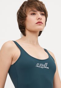 Maillot de bain teal avec de larges bretelles, arborant un logo blanc "O'Neill" à l'avant. Texture lisse, design athlétique et coupe ajustée.