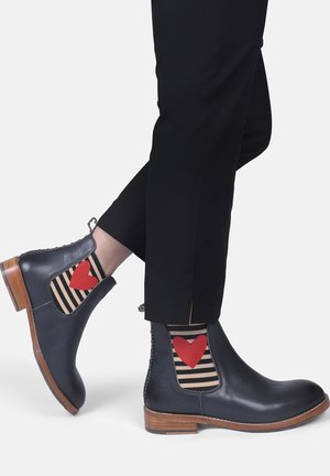 Bottines en cuir noir avec des panneaux latéraux élastiques, présentant un cœur rouge sur des chaussettes rayées et un talon en bois. La visibilité des chaussettes met en valeur le design.