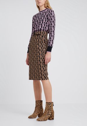 Femme portant un haut à manches longues rose et noir à motifs, une jupe marron et noire à motifs taille haute au genou, et des bottines à imprimé léopard.
