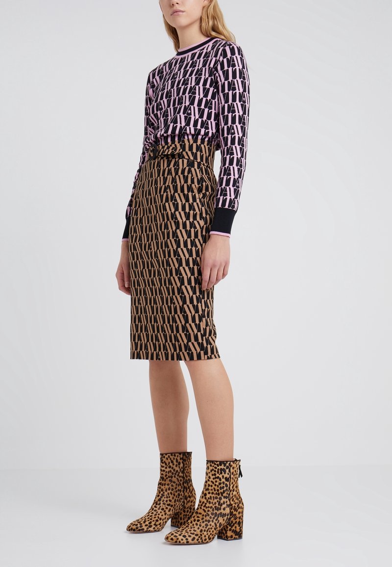 Femme portant un haut à manches longues rose et noir à motifs, une jupe marron et noire à motifs taille haute au genou, et des bottines à imprimé léopard.