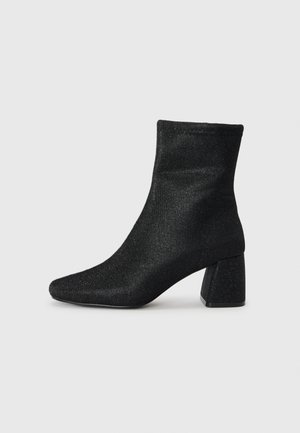 Black ankle boot with a textured, shimmering finish and a pointed toe. Features a chunky heel and a fitted shaft design.