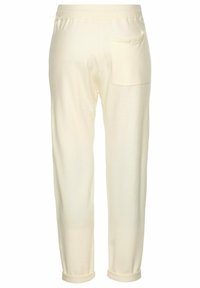 Helle cremefarbene Hosen mit weicher Textur, schmal zulaufenden Beinen und einer Gesäßtasche. Die Säume sind leicht hochgekrempelt.