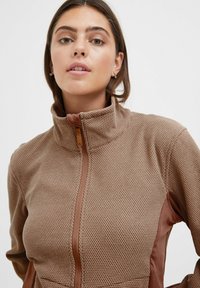 Brown zip-up jacket featuring a textured honeycomb pattern, with contrasting smooth brown accents on the collar and sides.