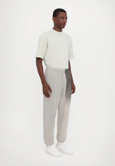 Light grey cotton t-shirt with short sleeves, paired with tapered sweatpants featuring a gradient from light to dark grey, worn with white sneakers.