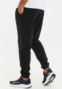 Zwarte fleecesportbroeken met zijzakken en elastische boorden, gecombineerd met zwart-witte sport sneakers. Soepele textuur, losse pasvorm.