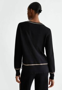 Maglione lavorato a maglia nero con maniche lunghe, caratterizzato da un accento dorato al collo e all'orlo, una texture a coste e una vestibilità rilassata.