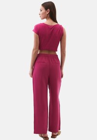 Lyhyet hihat, lyhyt paita ja leveälahkeiset housut magentavärisestä kankaasta. Paidassa on rento istuvuus; housuissa on joustava vyötärö ja taskut.