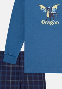 Blue long-sleeve shirt with a dragon graphic and the word "Dragon," paired with navy plaid pants featuring yellow lines. Cotton material, standard fit.