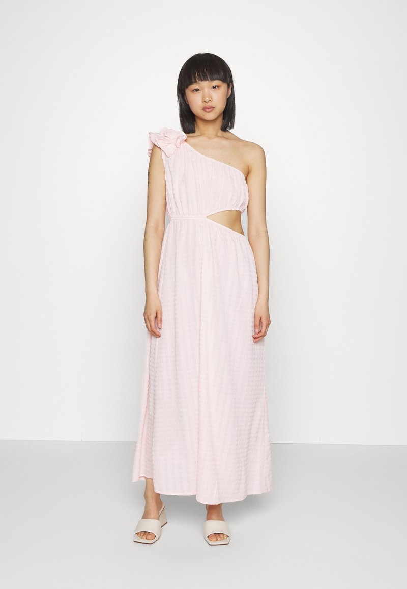 Vestido rosa de um ombro, com um tecido texturizado, apresentando um recorte na cintura e um detalhe floral no ombro. Silhueta longa e fluida.