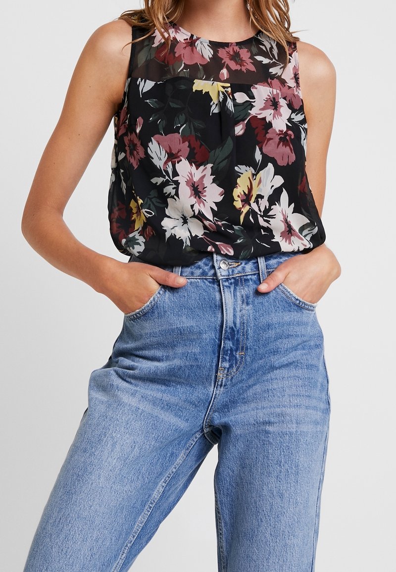 Floral tank top in black with a sheer panel, featuring pink, yellow, and green flowers; paired with high-waisted light blue jeans.
