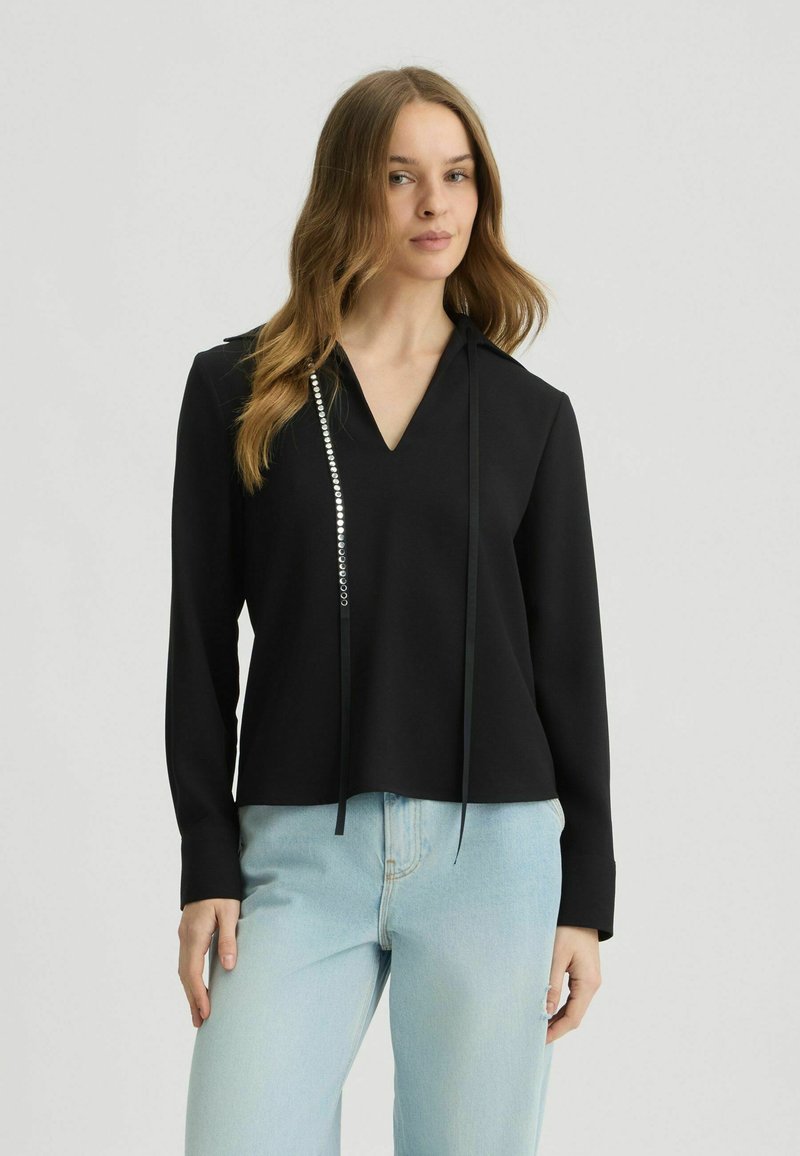 Zwarte top met een V-hals, voorzien van lange mouwen en een decoratieve strook met zilveren accenten aan één zijde. Glad stof, minimalistisch ontwerp.