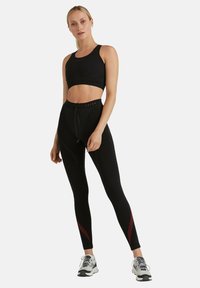 Czarny sportowy stanik i legginsy z wysokim stanem z czerwonymi ukośnymi paskami, wykonane z tkaniny odprowadzającej wilgoć. Posiadają pasek ze sznurkiem w talii.