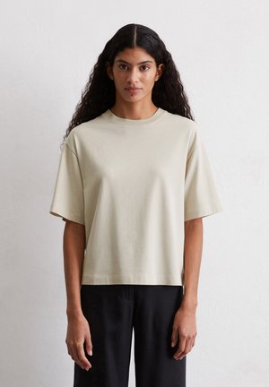 T-shirt a maniche corte, di un leggero colore beige, realizzato in tessuto morbido, con una vestibilità comoda e scollo rotondo, abbinato a pantaloni neri.