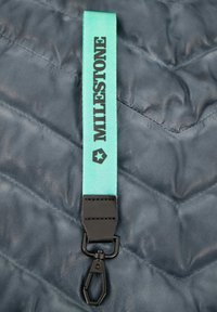 Lanyard aus mintgrünem Stoff mit schwarzem "MILESTONE"-Text, ausgestattet mit einem schwarzen Clip und strukturiertem Hintergrund.