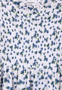 Tessuto bianco con un motivo floreale che presenta piccoli fiori blu e foglie verdi. La trama è spiegazzata con un design arricciato al collo.