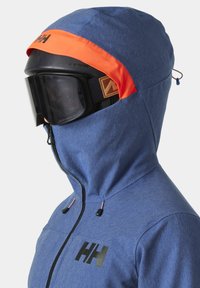 Blaue isolierte Jacke mit orangefarbenem Kapuzenbesatz, schwarzem Reißverschluss, Logo auf der Vorderseite und einer Skimaske, die mit einer Goggle integriert ist.