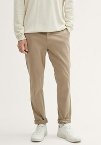 Beige chinos with a slim fit, featuring front pockets and rolled cuffs, paired with white sneakers and a light cream long-sleeve top.