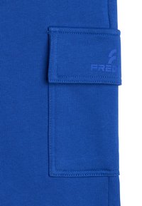 Tela azul con una superficie texturizada y un bolsillo con solapa que presenta acentos cosidos. Logo impreso en la zona del bolsillo.