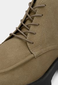 Bežiniai zomšiniai auliniai batai su lygiu paviršiumi, su raišteliais ir apvaliu pirštų galiuku, akcentuoti juodais guminiais padu.