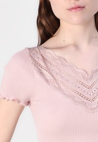 Ribbed, pale pink top with short sleeves, featuring a scalloped lace neckline and intricate detailing along the edges.
