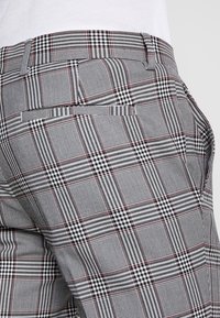 Spodnie w kratę w kolorze czarno-białym z czerwonym akcentem, z płaskim przodem i kieszeniami bocznymi, wykonane z teksturowanej tkaniny.