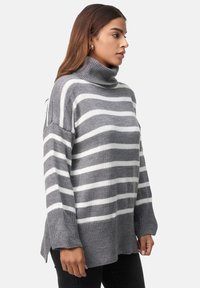 Grau-weißer gestreifter Rollkragenpullover mit lockerer Passform, geripptem Kragen und seitlichen Schlitzen am Saum. Weiche, gestrickte Textur.