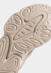 Beige sneakersula med upphöjda mönster, spår och cirkulära detaljer för grepp. Slät yta med kontrasterande räfflade sektioner.