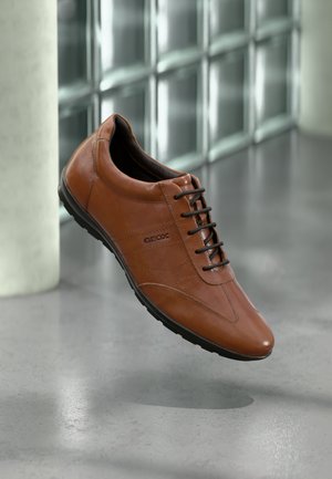 Bruine leren schoen met een gladde textuur, voorzien van een ronde neus, vetersluiting en een rubberen zool met een subtiel profiel.