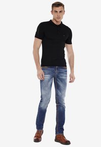 Polo noir à manches courtes avec un col et un logo sur la poitrine, associé à un jean skinny bleu délavé et des bottes marron à lacets.