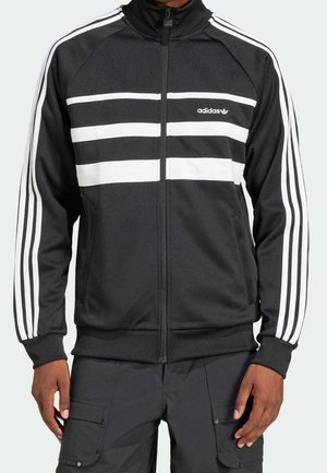 Veste de survêtement noire Adidas avec des bandes blanches sur les manches et la poitrine, fermeture éclair à l'avant et logo Adidas sur la poitrine gauche.