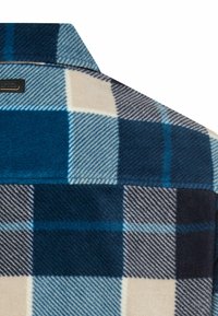 Blauw-witte geruite flanellen blouse met een zachte textuur, kraag en zwart label, gezien van achteren.