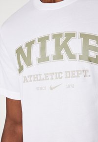 T-shirt bianco in cotone con una grafica audace in verde oliva "NIKE" con "ATHLETIC DEPT." sotto, impreziosito da un branding sottile e l'anno "1972."