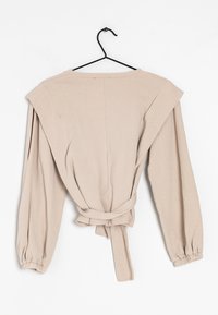 Beige Oberteil mit langen Ärmeln, lockerer Passform, weitem Schulterdesign und gebundenem Taillenzug. Weicher Stoff und elastische Bündchen.