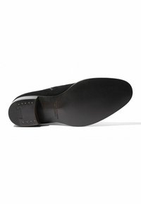 Suela de zapato de ante negro con un acabado liso negro, punta redondeada y remaches metálicos para agarre. Las marcas incluyen el nombre de la marca y detalles de tamaño.