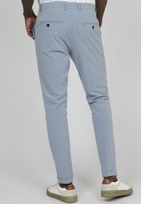 Pantalones ajustados de color azul claro con dos bolsillos traseros que tienen botones negros, un diseño de corte slim y puños enrollados, combinados con zapatillas blancas.