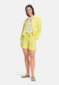 Linen blend yellow jacket and shorts set features a collared jacket, button closure, and tie-waist shorts. Paired with metallic sandals.