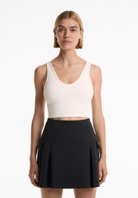 Beige cropped tank top with a textured pattern, paired with a black pleated skirt featuring side pockets and a fitted waistband.
