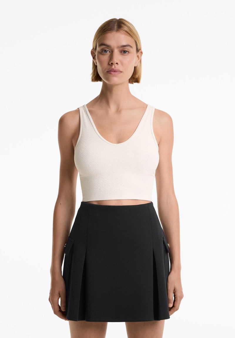 Beige cropped tank top with a textured pattern, paired with a black pleated skirt featuring side pockets and a fitted waistband.