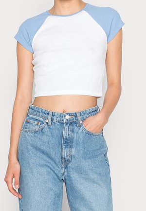 Obcięty biały t-shirt z jasnoniebieskimi raglanowymi rękawami, wykonany z miękkiej bawełny, zestawiony z jasnoniebieskimi dżinsami z wysokim stanem.