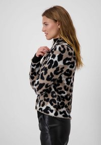 Leoprint-Pullover in Beige und Schwarz, aus weichem Material, mit lockerem Schnitt und Rundhalsausschnitt, kombiniert mit schwarzen Hosen.